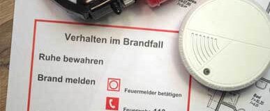 Feuerlöscher, Rauchmelder und Merkblatt „Verhalten im Brandfall“ auf einem Tisch