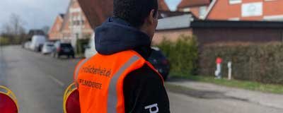 Mitarbeiter in Warnweste mit Aufdruck steht an Straßensperre mit Leitbaken in Wohnstraße