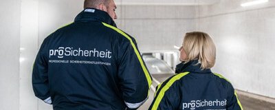 Zwei Sicherheitsmitarbeiter in ProSicherheit-Jacken stehen in einer Tiefgarage und sprechen miteinander